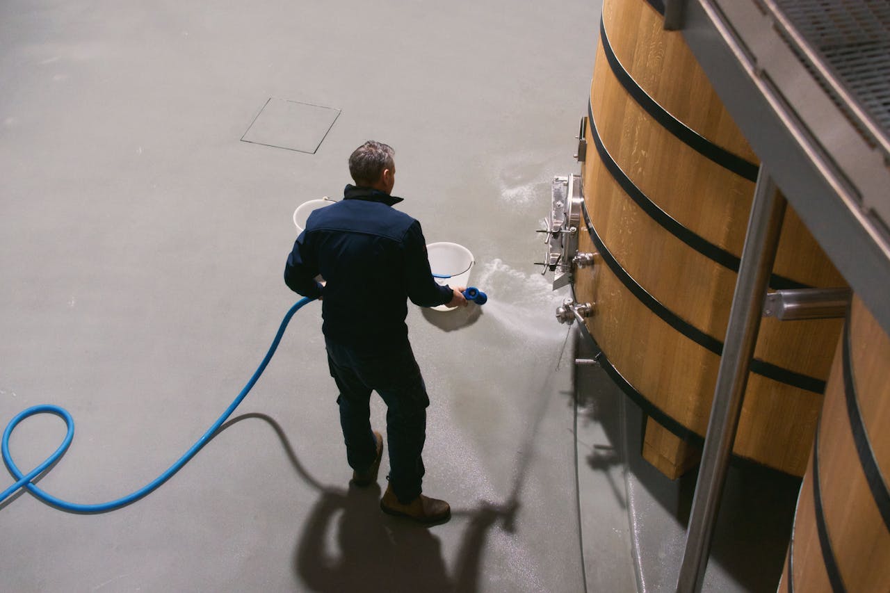 A winemaker cleans oak barrels in a Pauillac wine cellar in France, using a hose to maintain hygiene.